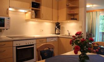A modern kitchen with wooden cabinets and light walls. On the table is a vase with red flowers.