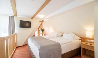 A cozy bedroom with a large bed and bright walls. There is a television and a nightstand with a lamp.