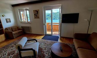 A cozy living room with a sofa, an armchair, and a round table. Large windows offer a beautiful view of the lake and the surrounding nature.