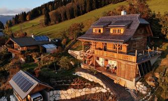 A picturesque, timber-clad house in a hilly landscape. The garden and the surrounding nature add a serene atmosphere to the scene.