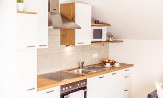 A modern kitchen with white cabinets and wooden surfaces. The equipment includes a stove, a sink, and a microwave.