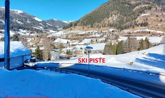 A snowy landscape with a ski slope in the background. In the foreground, there is a parking lot.