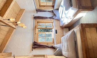 A cozy bedroom with two wooden beds. Large windows let in plenty of daylight and provide a view of nature.