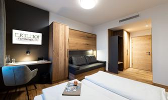 A modern room with wood paneling and a comfortable sleeping area. The room features a desk, a sofa, and a warm, inviting color tone.