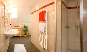A modern bathroom with a shower and two sinks. The walls are brightly tiled, and some towels are hanging decoratively.