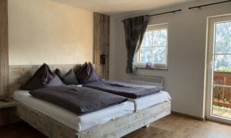 A cozy bedroom with a double bed and wooden furniture. Daylight enters the room through the window.