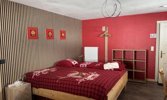 A cozy room with a large bed and a red hue.  
Walls with wood paneling and wall art give the space character.