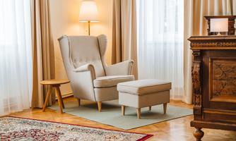 A cozy armchair with an ottoman in a bright room. Soft curtains and a rug create an inviting atmosphere.