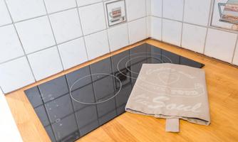 A modern cooking plate with two cooking zones on a wooden floor. Next to it lies a dish towel with the print "Food for the Soul."