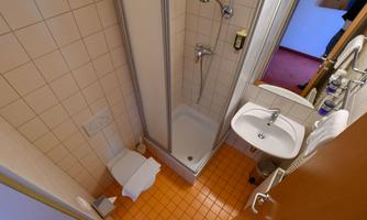 A small bathroom with a shower, sink, and toilet. The floor is equipped with orange tiles.
