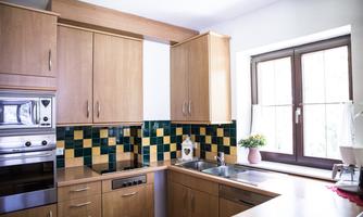 A bright kitchen with wooden cabinets and colorful tiles. The window lets in plenty of light, and there is a small plant on the countertop.