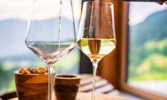 A glass of white wine is poured from a bottle into an elegant wine glass. In the background, a beautiful view and a cozy atmosphere can be seen.