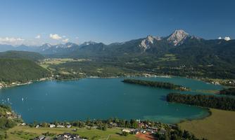 A beautiful lake surrounded by mountains and green meadows. The calm water surface reflects the clear sky.
