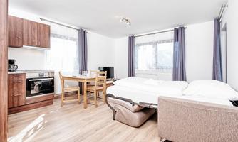 A modern apartment with a kitchenette, a dining area, and a sleeping area. Large windows provide plenty of natural light.
