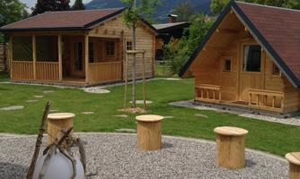 Two cozy wooden cabins stand in a green landscape. Surrounded by gravel and benches, the place offers a relaxed atmosphere.