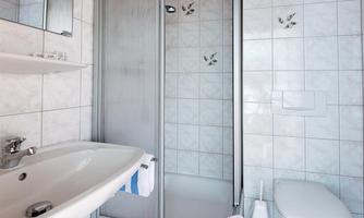 A modern bathroom with a shower cubicle, a sink, and a toilet. The walls are tiled, and the floor has a blue covering.