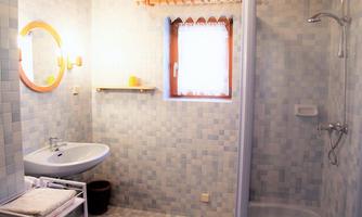A bright bathroom with blue tiles and a sink. There is a shower and a window that lets in daylight.