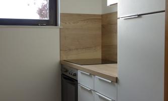 A modern kitchen with white cabinets and wooden accents. A window lets in natural light.