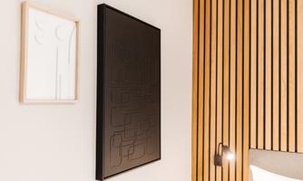 A modern room with wooden paneling and two pictures on the wall. The large picture is dark and textured, while the smaller picture has a minimalist white frame.