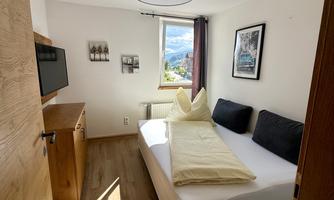 A bright bedroom with a large bed and two pillows. Pictures hang on the wall, and a television is available.