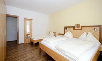 A simple room with two beds and a wooden floor. The walls are painted light and there is a mirror in the background.