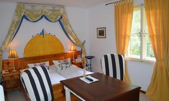 A cozy bedroom with a double bed and a bright color scheme. The decor includes a desk and two striped chairs.