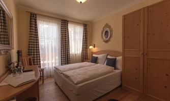 A cozy bedroom with a double bed and large windows. The walls are painted in warm colors, and there are wooden details as well as soft curtains.