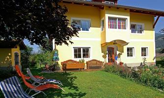 A light yellow house with a beautiful garden and colorful flowers. Nearby, there are deck chairs on the green lawn.