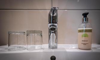 A modern wash station with a shiny faucet and two glasses. Next to it is a soap bottle from Abbot & Broome.