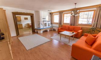 A cozy living room with orange sofas and a wooden floor. Large windows provide plenty of daylight and an inviting atmosphere.