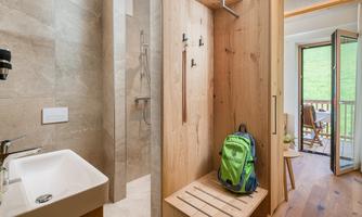 A modern bathroom with a shower and a wooden sink. In the foreground is a backpack and an open door leads to a balcony.