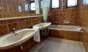 A bathroom with two sinks, a bathtub, and a shower. The walls are tiled with brown tiles and there are windows with curtains.