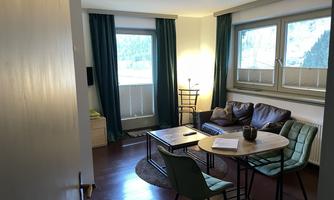 A cozy room with a sofa and a table. Large windows let in natural light and create an inviting atmosphere.