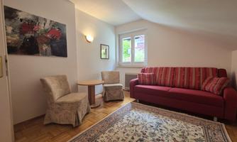 A cozy living space with a red sofa and two chairs. A painting is hanging on the wall, and a rug is on the floor.