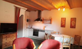 A cozy holiday apartment with an open kitchen and a dining area. The furniture is simple and inviting, with a television and some decorative pictures on the walls.