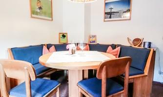 A cozy dining area with a round table and benches. Pictures hang on the wall, and the lighting creates a pleasant atmosphere.