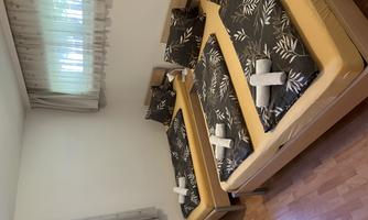 A cozy bedroom with two single beds and decorative bedding. The room has bright colors and large windows for daylight.