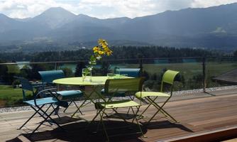 A beautiful table with colorful chairs on a terrace. In the background, mountains and a green landscape can be seen.