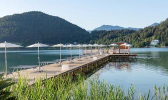 A dock at the shore of a calm lake, surrounded by mountains. Awnings and lounge chairs invite relaxation.