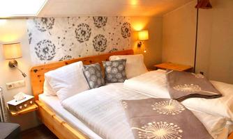A cozy bedroom with a double bed and soft pillows. The walls are decorated with floral patterns and there is soft light from wall lamps.