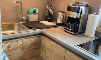 A modern kitchen with wooden paneling and an elegant countertop. Visible are a sink, various kitchen appliances, and kitchen utensils.