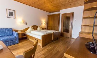 A cozy room with wooden paneling and a double bed. There is a small desk, a couch, and a wardrobe.