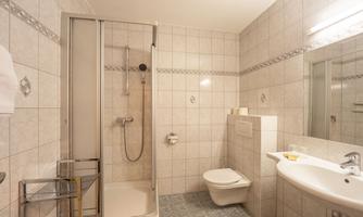 A modern bathroom with a shower, toilet, and sink. The walls are light tiled, and there is a clear, functional design.