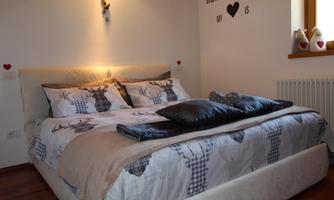 A cozy bedroom with a large, inviting bed and decorative pillows. Hearts hang on the wall and a warm light creates a pleasant atmosphere.