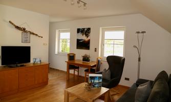 A modern living room with a TV, a table, and chairs. The large windows let in plenty of light and create an inviting atmosphere.