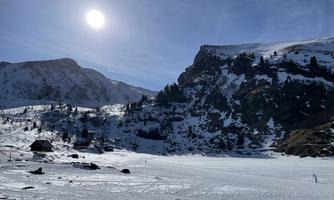 A snowy landscape with mountains and a clear sky. The sun shines brightly over the winter landscape.