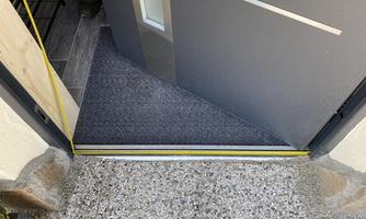 An entrance door with a rug in front of it. The floor is made of gray stone and a measurement is visible.