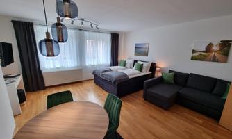 A modern and cozy room with a double bed and a couch. The room has large windows, a dining table, and is stylishly furnished.