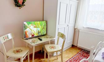 A cozy room with a television on a small table and two chairs. A white cabinet stands against the wall and the floor is covered with a colorful rug.
