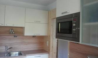 A modern kitchen with white cabinets and wooden surfaces. The microwave is integrated into the wall and there is a stainless steel sink.